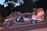 The wreckage of a silver Ford sedan after crashing into trees.