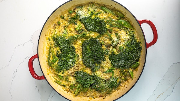 Dutch oven pot with spring vegetable orzo, topped with dill and generous dollops of pest.
