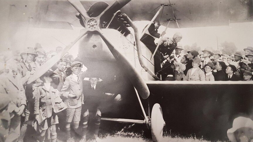 Aged photo of Lieutenant Long's biplane on the ground at Highfield, surrounded by schoolkids
