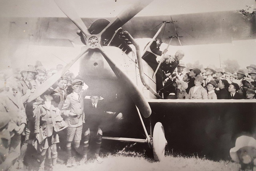 Aged photo of Lieutenant Long's biplane on the ground at Highfield, surrounded by schoolkids