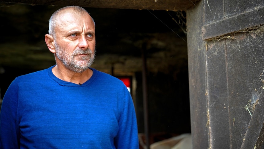 A man stands in the doorway of an outbuilding, looking on.