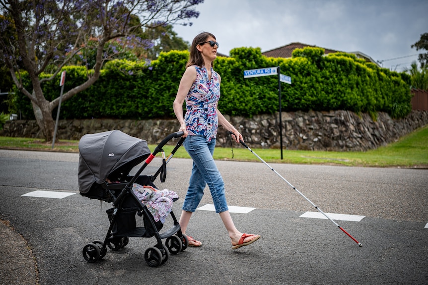 Jennelle walking down a suburban street with a cane, pulling a pram alongside her.