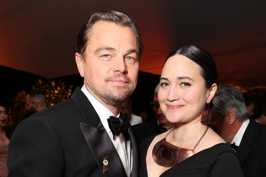 Leonardo DiCaprio in a suit with bow tie, Lily Gladstone with Native jewellery and a black dress smiling