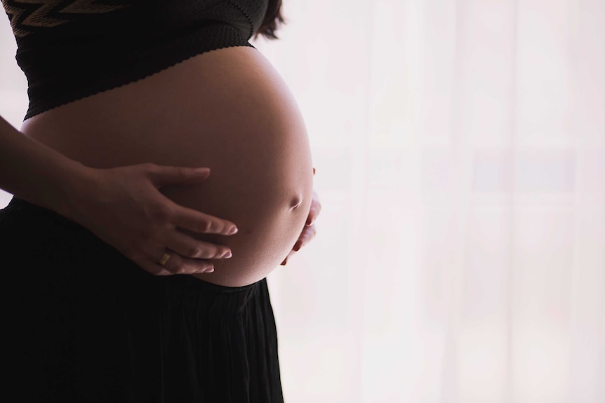 Heavily pregnant woman holds her bare stomach.