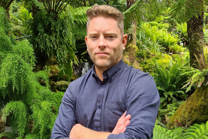 A man crossing his arms in front of a rainforest