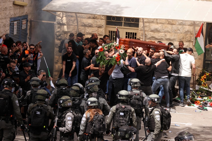 Israeli security forces back people holding up a coffin against a wall.