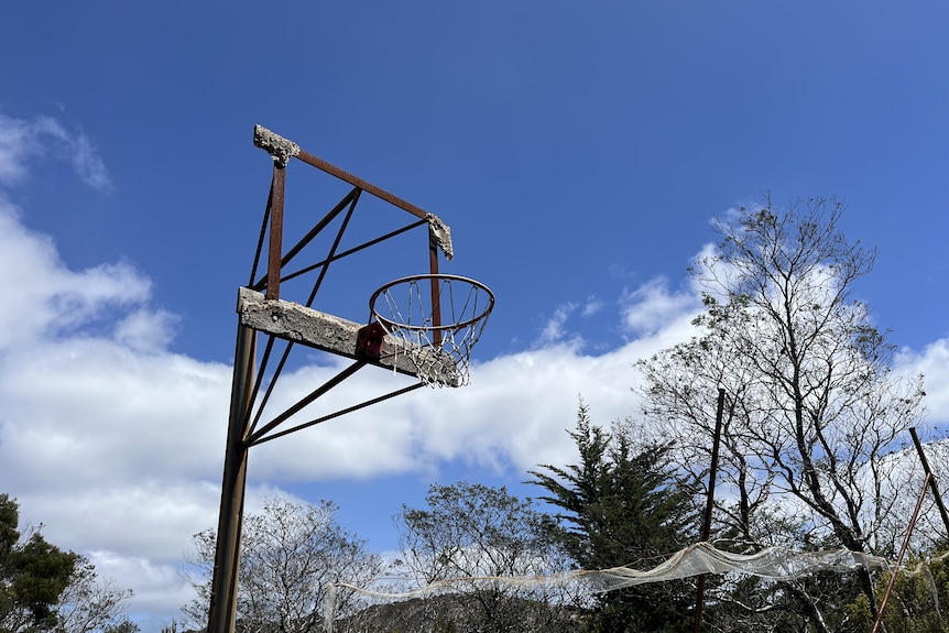 A decayed old basketball hoop on a blue sky.