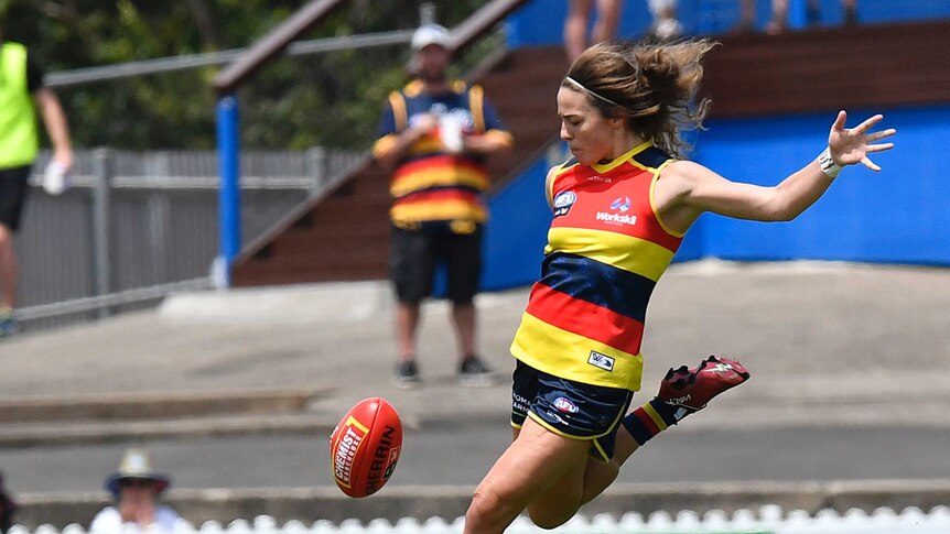 Jenna McCormick prepares to kick an AFLW football wearing a blue, red and yellow striped singlet
