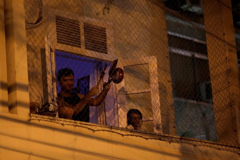 A man on his balcony, banging pans with a spoon.