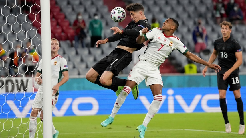 A German footballer jumps up and nods the ball down into the net from near the goalline.