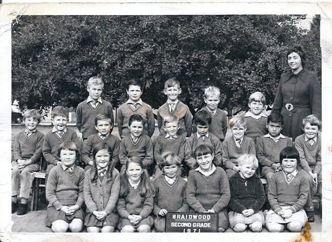 A black and white photo of a class of second grade children in v-neck sweaters and their teacher