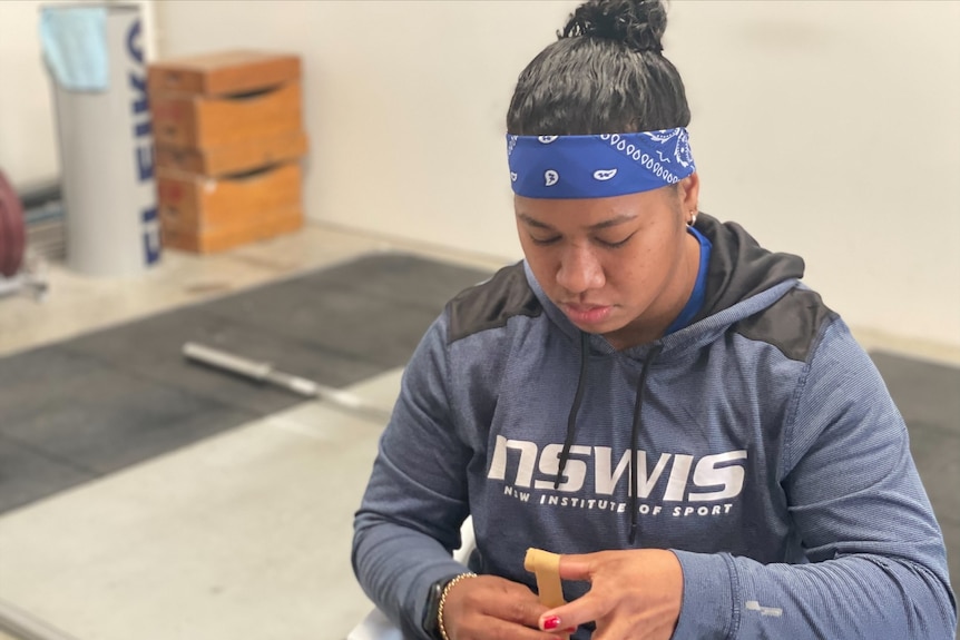 Eileen Cikamatana, wearing a blue headband and grey top, looks down while adjusting the tape on her thumb.