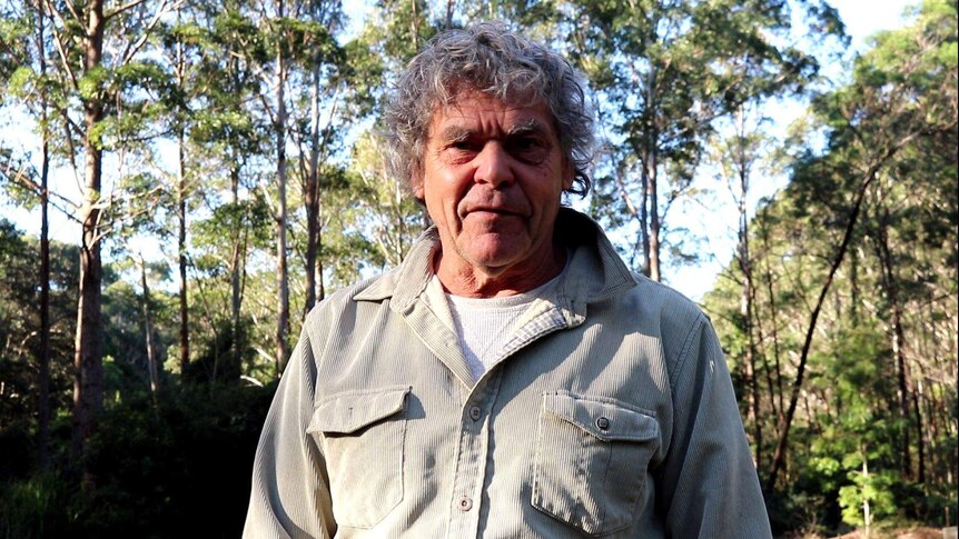 Indigenous elder Noel Butler stands outside surrounded by trees. He looks into the camera. 