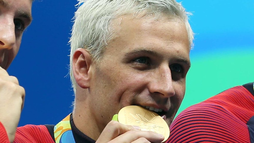 Blonde US swimmer Ryan Lochte bites on a gold medal.