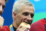 Blonde US swimmer Ryan Lochte bites on a gold medal.