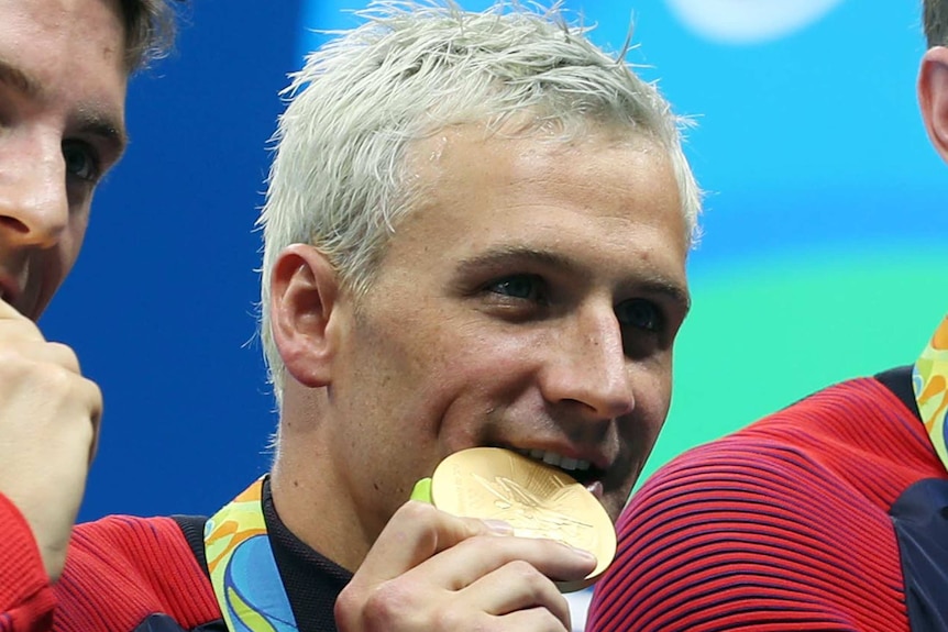 Blonde US swimmer Ryan Lochte bites on a gold medal.