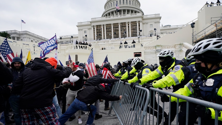 Rioters at the capitol push against a police barricade, Capitol building in the background