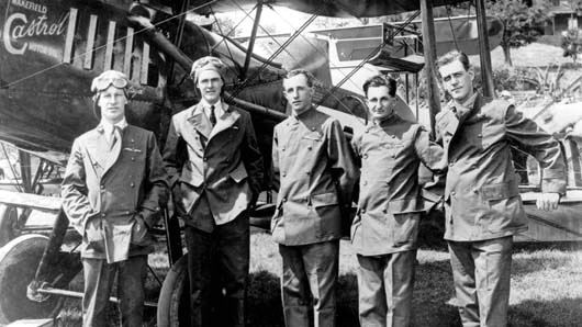 A black and white image of people standing in front of an old fashioned plane