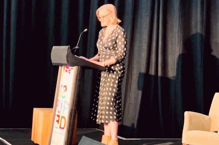 Leigh Sales stands at a podium in a black and white polka dot dress.