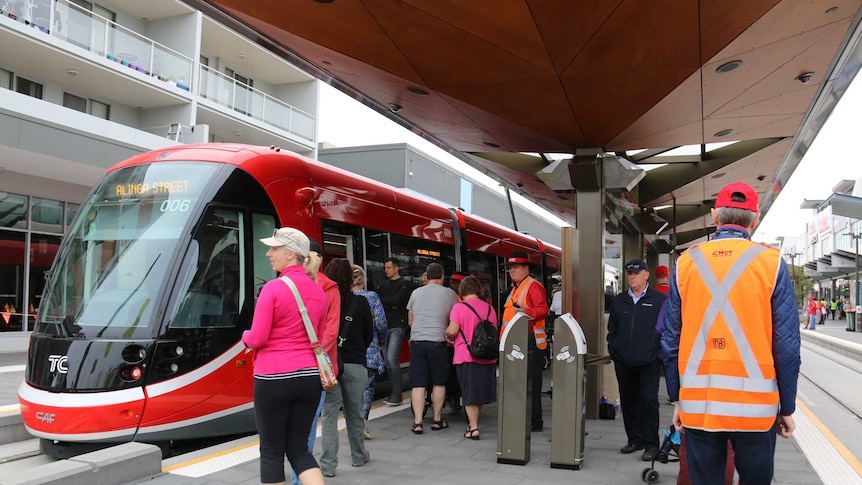People walking towards a light rail vehicle on a platform in Canberra on an overcast day.
