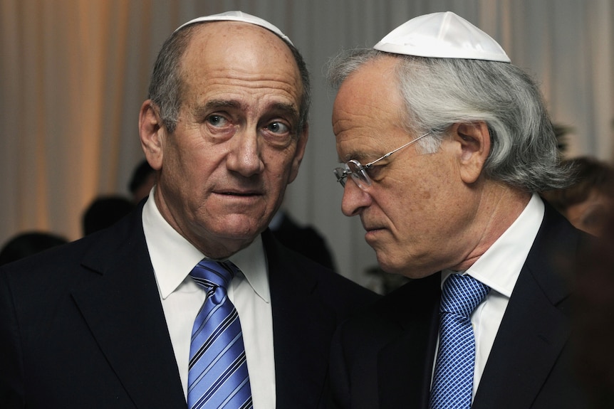 Ehud Olmert and Martin Indyk, both wearing skullcaps and in conversation, speaking with faces close together.