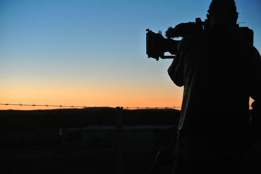 Silhouette of ABC cameraman filming a sunset and brilliant blue sky.