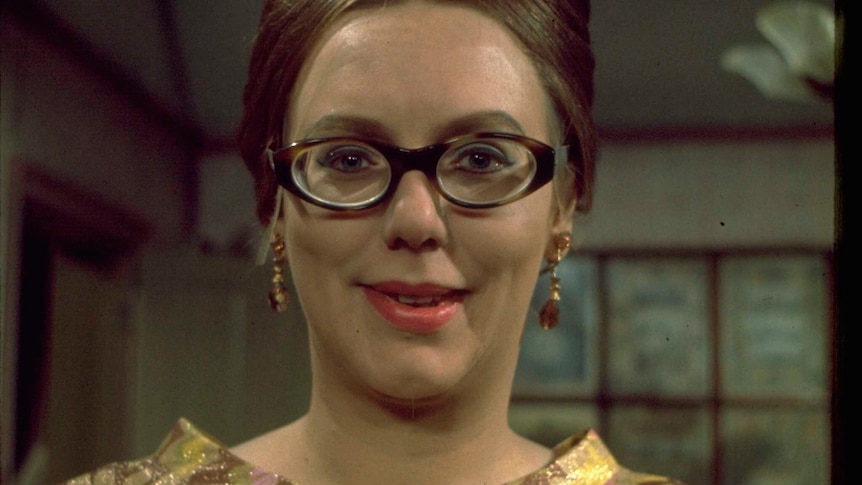 A younger Anna Karen wearing glasses, dangling earrings and her hair knotted in a bun on top of her head