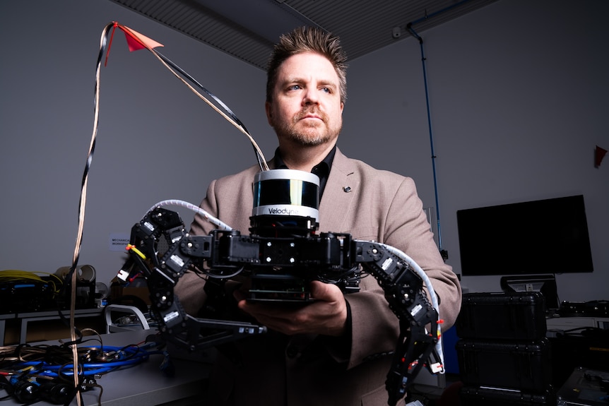 A man holds a black and white robot with curved legs and a camera on top