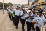 AFP officers in the Solomon Islands, some with drums and horns, march down a street in Honiara waving at people.