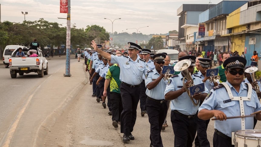 AFP officers in the Solomon Islands, some with drums and horns, march down a street in Honiara waving at people.