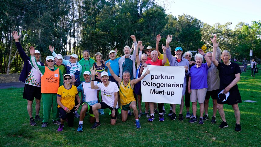 A group of octogenarians hold up a sign saying 'parkrun octogenarian meet-up' and smile.