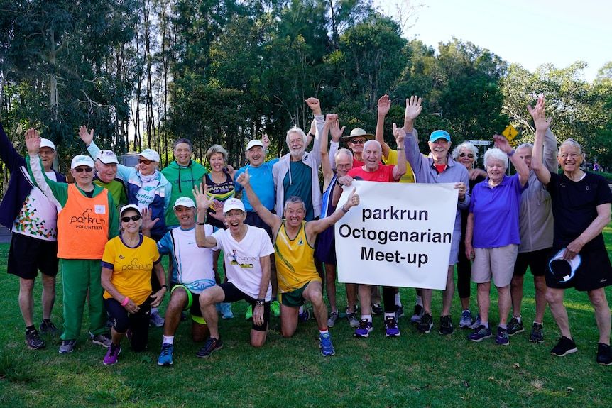 A group of octogenarians hold up a sign saying 'parkrun octogenarian meet-up' and smile.