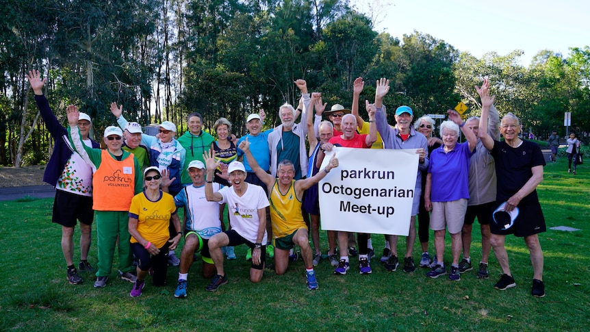 A group of octogenarians hold up a sign saying 'parkrun octogenarian meet-up' and smile.