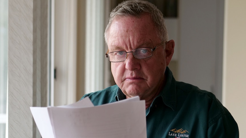 A seated Kevin Barracough wearing glasses looks out from behind a financial document