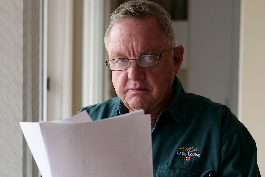 A seated Kevin Barracough wearing glasses looks out from behind a financial document