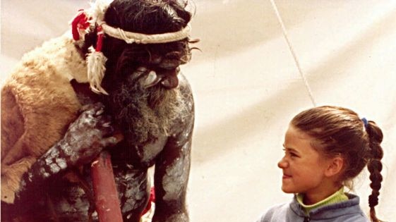 An Aboriginal dancer shows a young girl how to play the didgeridoo.