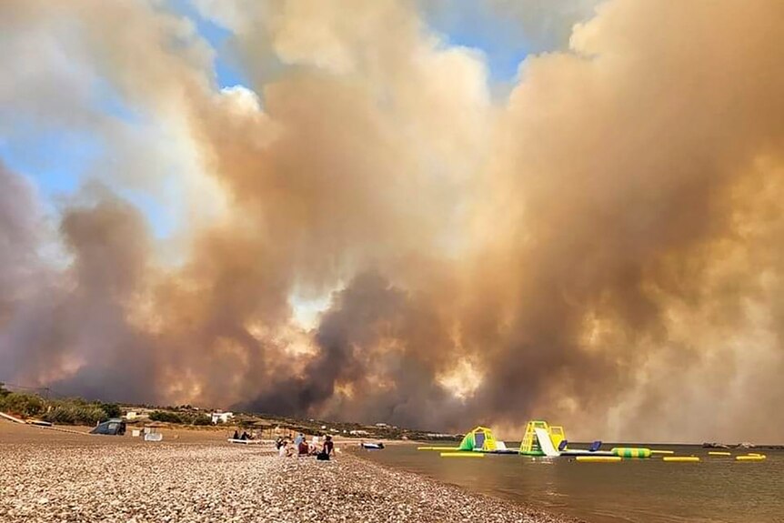 Wildfire smoke rises above an evacuated beach on the island of Rhodes