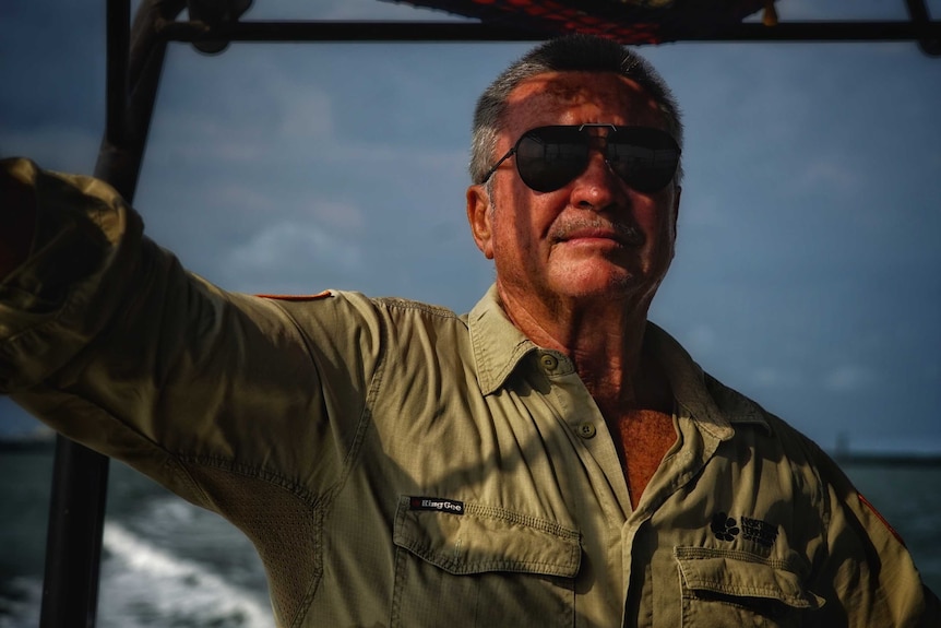 Un homme en lunettes de soleil aviateur regarde depuis un bateau.