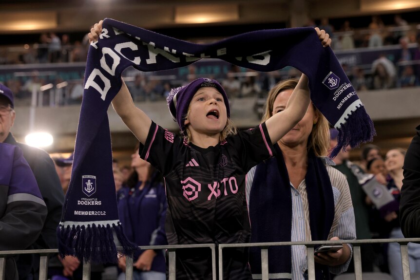 A boy holds up a purple scarf while chanting at a football match