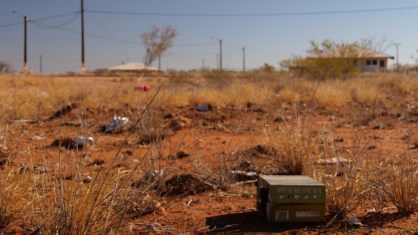 Old beers cans and boxes of wine are littered on the red dirt.
