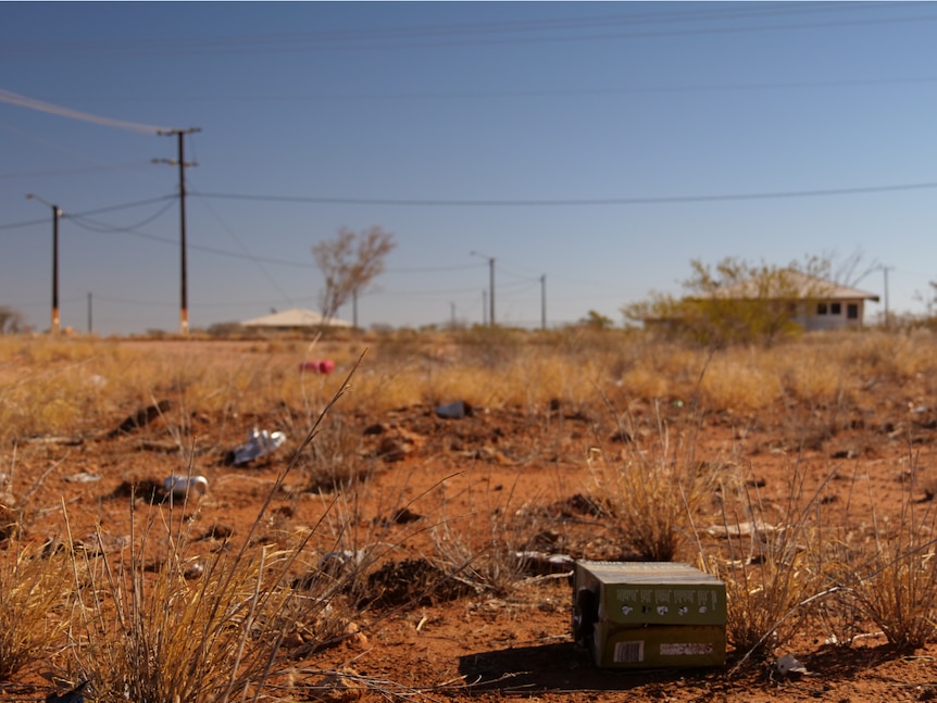 Old beers cans and boxes of wine are littered on the red dirt.