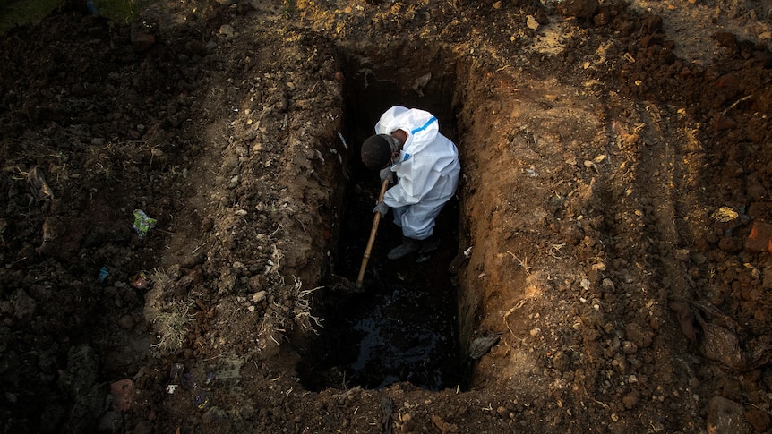 A man in protective gear digs a deep grave