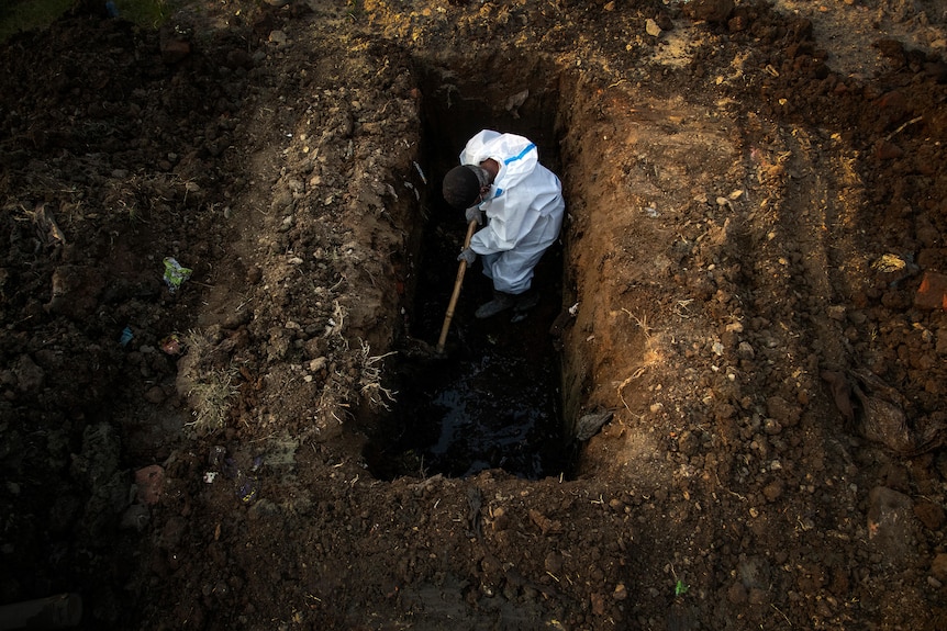 A man in protective gear digs a deep grave
