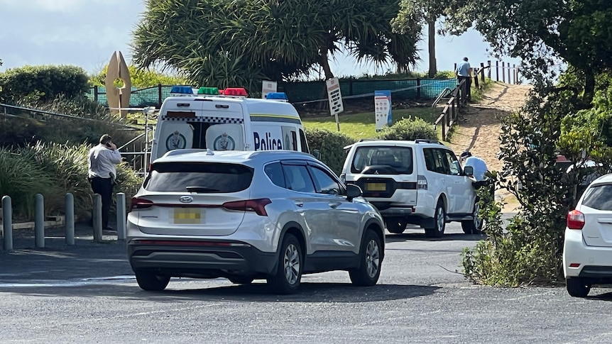Police vehicle in a beach carpark with officers in the background