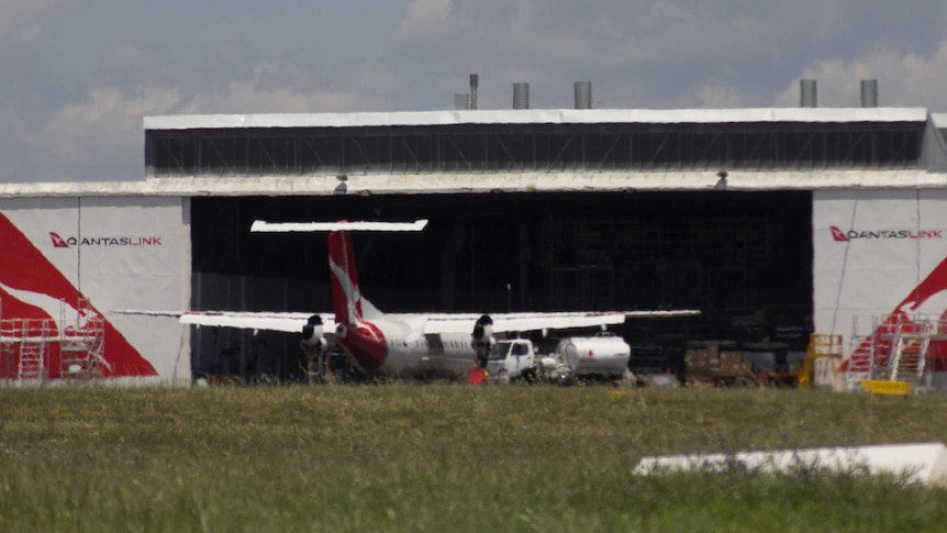 View across the tarmac to a huge workshop hanger with Qantas logos, and a plane parked in front