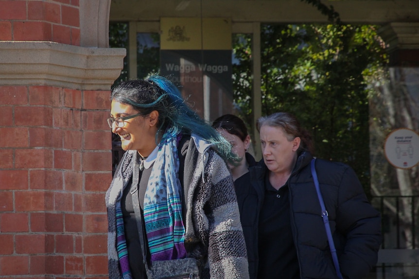 Two women, one with black hair and a blue streak, the other with brown hair leave a court house. 