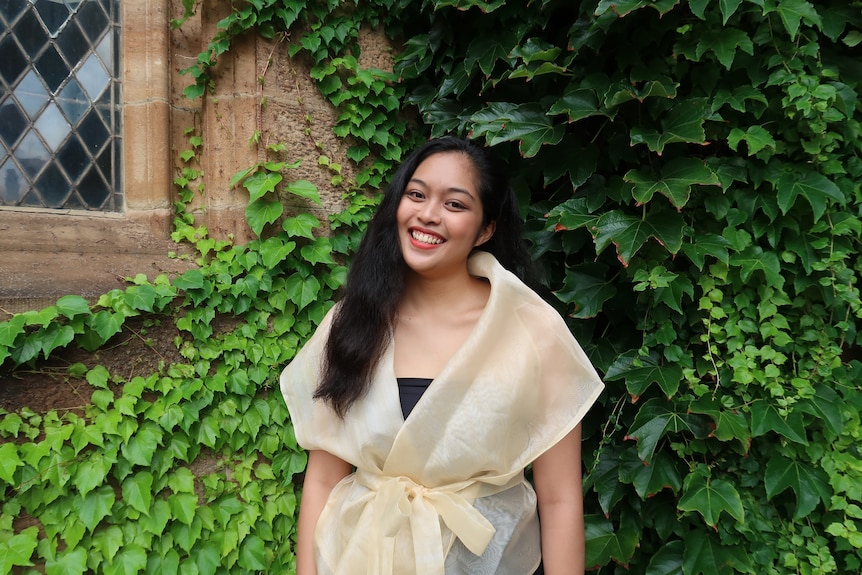 Sophia Maranan stands in front of a wall covered in vines smiling. 