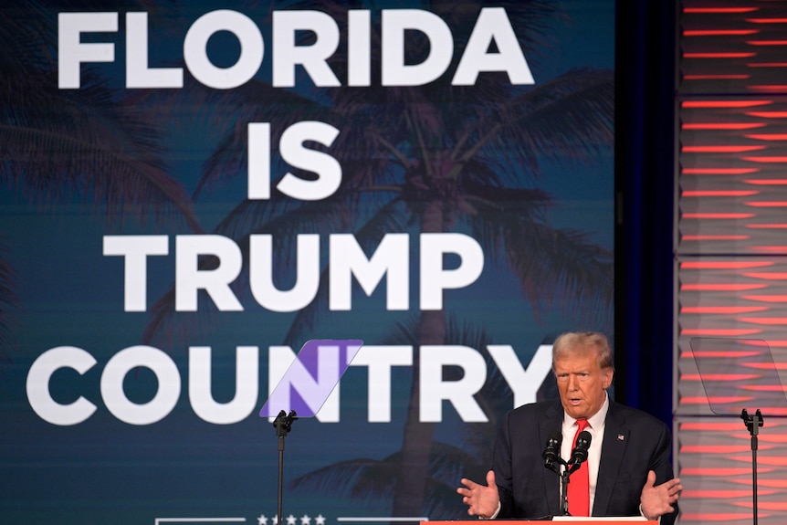 Donald Trump speaks on stage in front of Florida is Trump country sign