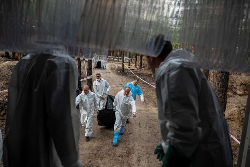 Members of the Ukrainian Emergency Service carry the exhumed body of a person to a truck at a site of a mass burial.