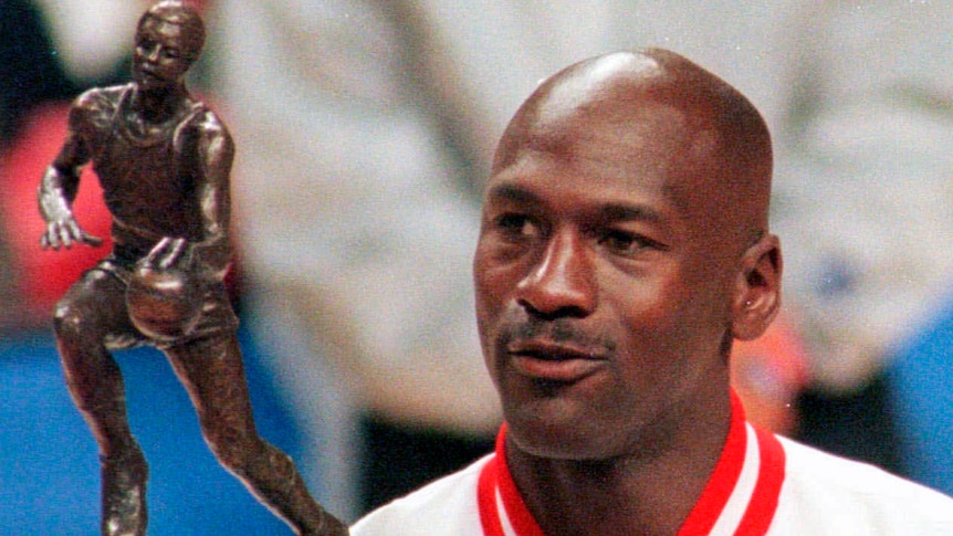 Michael Jordan, wearing his Chicago Bulls warm-up tracksuit, holds up the trophy as the NBA MVP in 1998.